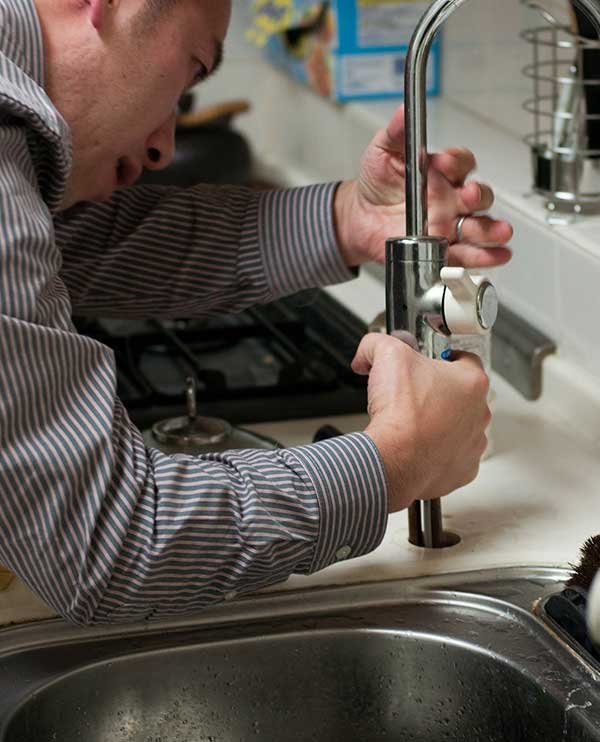 A man repairing a leaking pipe under a sink with a wrench